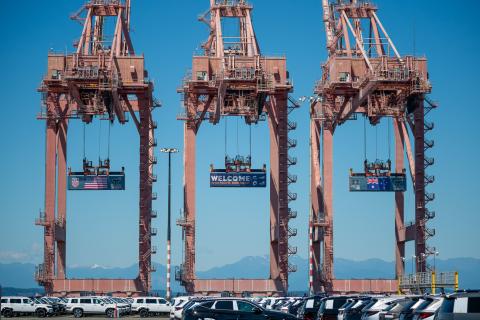Three containers hang from cranes at Terminal 46 in Seattle. The middle container has a “Welcome to the Pacific Northwest” message to FIFA World Cup visitors, while the outside containers have the U.S. and Australian flags.