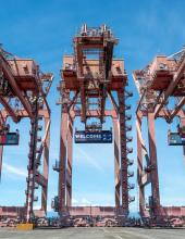 Three containers hang from cranes at Terminal 46 in Seattle. The middle container has a “Welcome to the Pacific Northwest” message to FIFA World Cup visitors, while the outside containers have Belgium and Egypt’s flags.