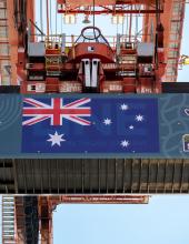 A shipping container with an Australia flag banner hangs from a crane at Terminal 46 in Seattle.