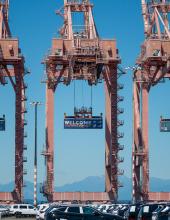 Three containers hang from cranes at Terminal 46 in Seattle. The middle container has a “Welcome to the Pacific Northwest” message to FIFA World Cup visitors, while the outside containers have the U.S. and Australian flags.