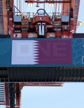 A shipping container with a Qatar flag banner hangs from a crane at Terminal 46 in Seattle.