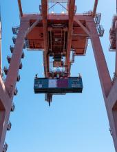 A shipping container with a Qatar flag banner hangs from a crane at Terminal 46 in Seattle.