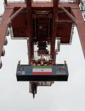 A shipping container with an Iran flag banner hangs from a crane at Terminal 46 in Seattle.