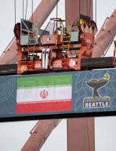 A shipping container with an Iran flag banner hangs from a crane at Terminal 46 in Seattle.