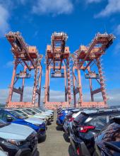 Three containers hang from cranes at Terminal 46 in Seattle. The middle container has a “Welcome to the Pacific Northwest” message to FIFA World Cup visitors, while the outside containers have the United States flag.
