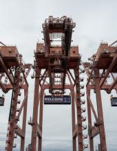 Three containers hang from cranes at Terminal 46 in Seattle. The middle container has a “Welcome to the Pacific Northwest” message to FIFA World Cup visitors, while the outside containers have the United States and Belgium flags.