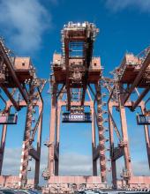 Three containers hang from cranes at Terminal 46 in Seattle. The middle container has a “Welcome to the Pacific Northwest” message to FIFA World Cup visitors, while the outside containers have the United States flag.