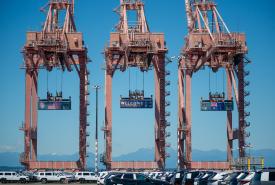 Three containers hang from cranes at Terminal 46 in Seattle. The middle container has a “Welcome to the Pacific Northwest” message to FIFA World Cup visitors, while the outside containers have the U.S. and Australian flags.